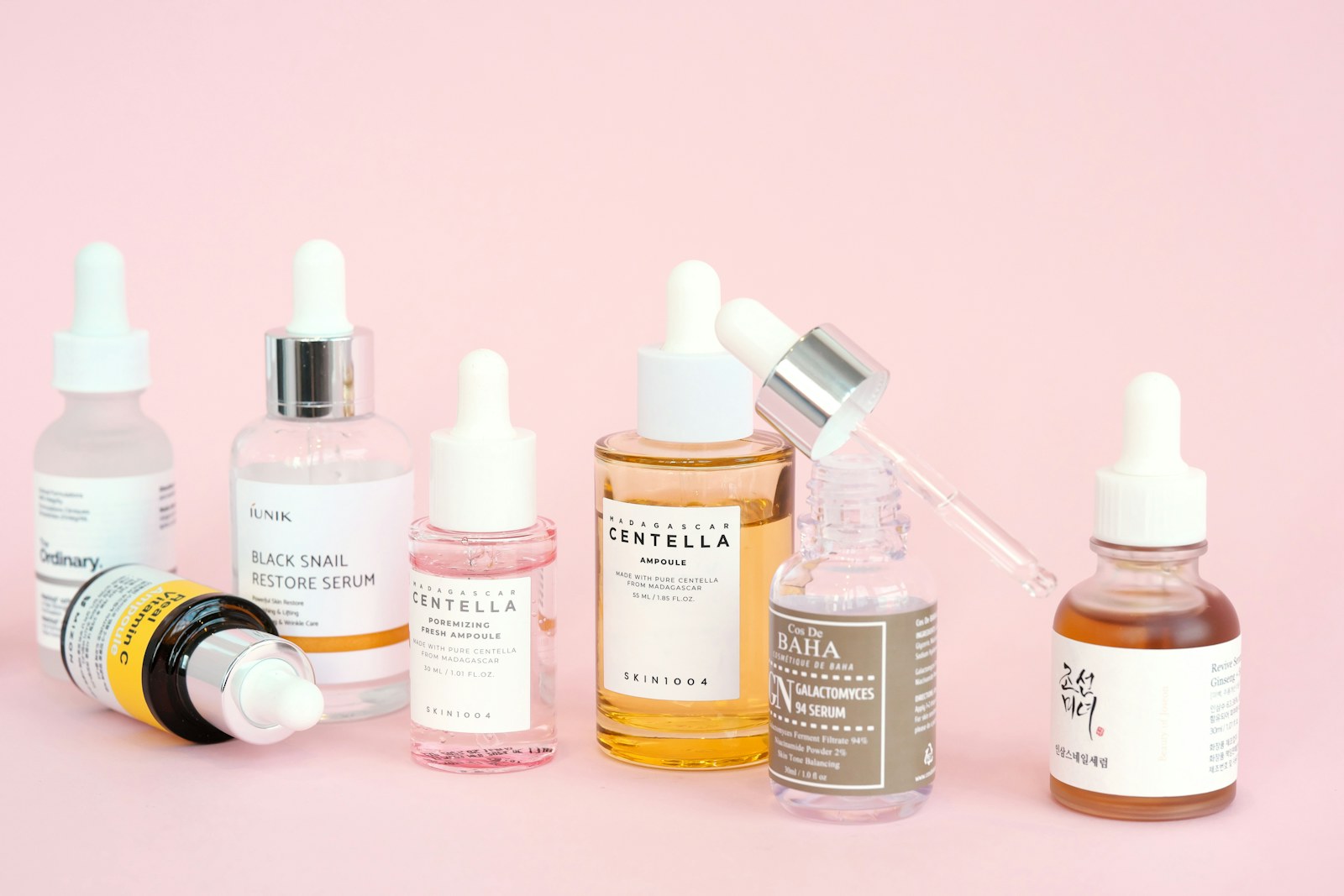 Finished cosmetic skincare serums and dropper bottles arranged on a pink surface